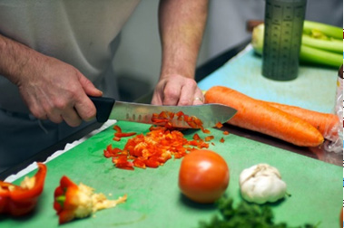 A person chopping red bell pepper on a green cutting board with other vegetables nearby. - International Hotel School