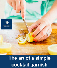 A person slicing a lemon into circular garnishes for cocktails on a wooden cutting board. - International Hotel School