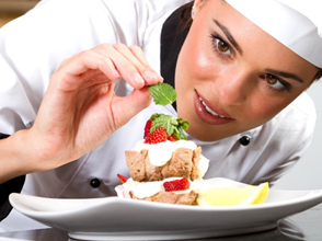 A chef garnishing a dessert with strawberries and mint leaves on a white plate. - International Hotel School