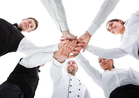 Group of hospitality staff members joining hands in a circle, showcasing teamwork and collaboration. - International Hotel School