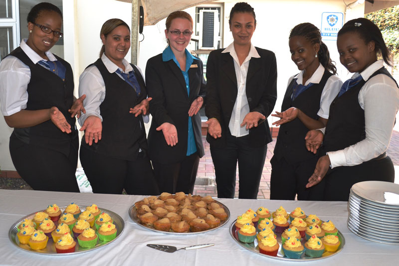 Group of hospitality students presenting a platter of colorful cupcakes and muffins at an event. - International Hotel School