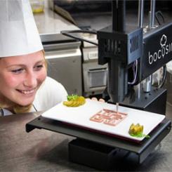 A chef observing a Bocusini food printer while preparing a dish in a kitchen. - International Hotel School