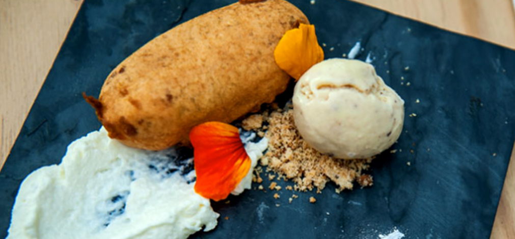 A dessert plate featuring a fried cake, ice cream, and garnishes on a slate surface. - International Hotel School