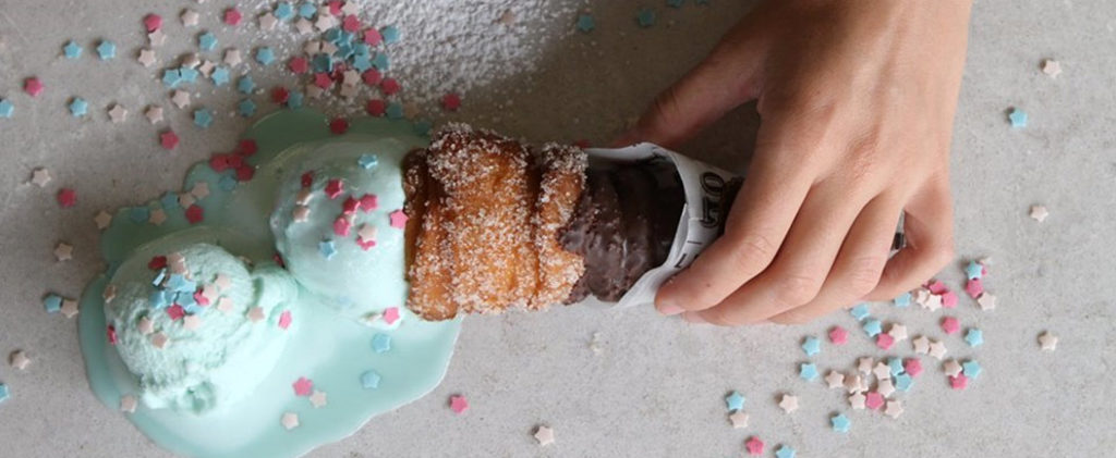 Hand holding an ice cream cone with three scoops of ice cream and colorful sprinkles. - International Hotel School
