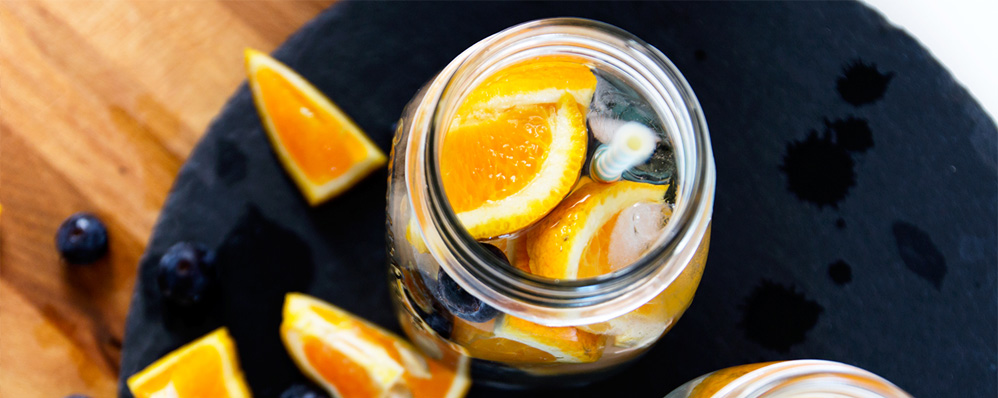 Infused water with orange slices and blueberries in a glass jar on a slate surface. - International Hotel School