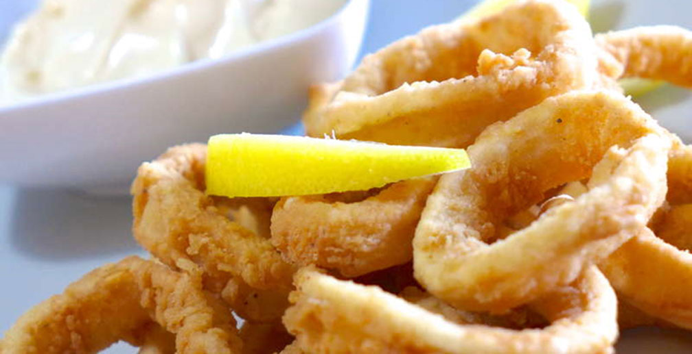 Plate of deep fried calamari rings garnished with a lemon slice and served with a dipping sauce. - International Hotel School