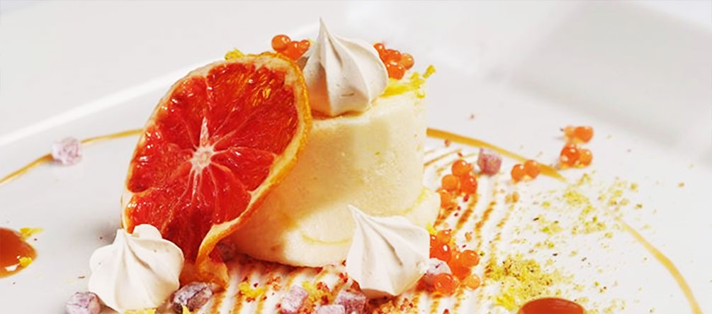 A dessert featuring a round cream base topped with a slice of citrus and decorative elements. - International Hotel School