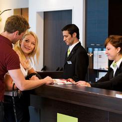 A couple interacting with hotel reception staff at a modern hotel front desk. - International Hotel School