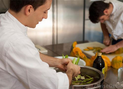 Two male sous chefs working in a kitchen, one peeling vegetables and the other chopping on a cutting board. - International Hotel School