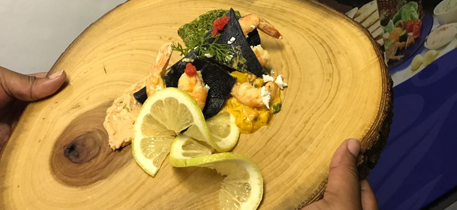 Plate of pasta with squid ink, prawns, and garnishes served on a wooden platter. - International Hotel School