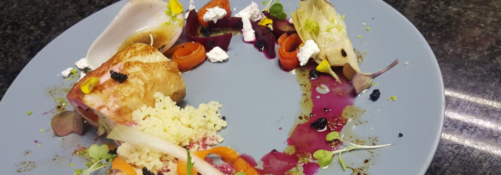 A gourmet dish featuring chicken, pickled vegetables, and couscous on a blue plate. - International Hotel School