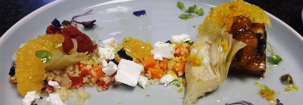 A plated dish featuring grilled chicken, couscous, and citrus garnishes. - International Hotel School
