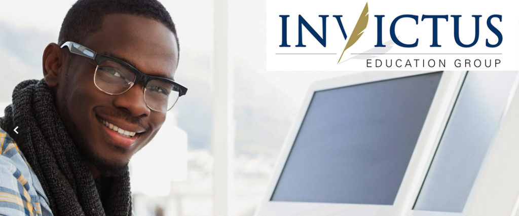 A young man wearing glasses and a scarf, smiling while sitting at a computer desk. - International Hotel School