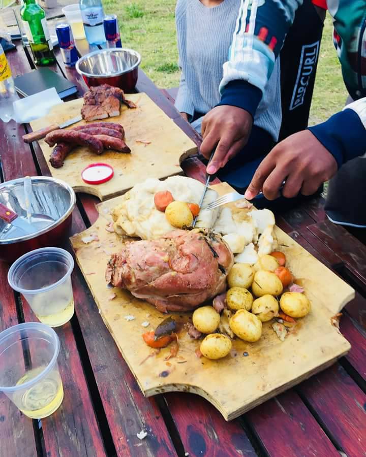 A person slicing cooked meat on a wooden board with vegetables and drinks nearby. - International Hotel School
