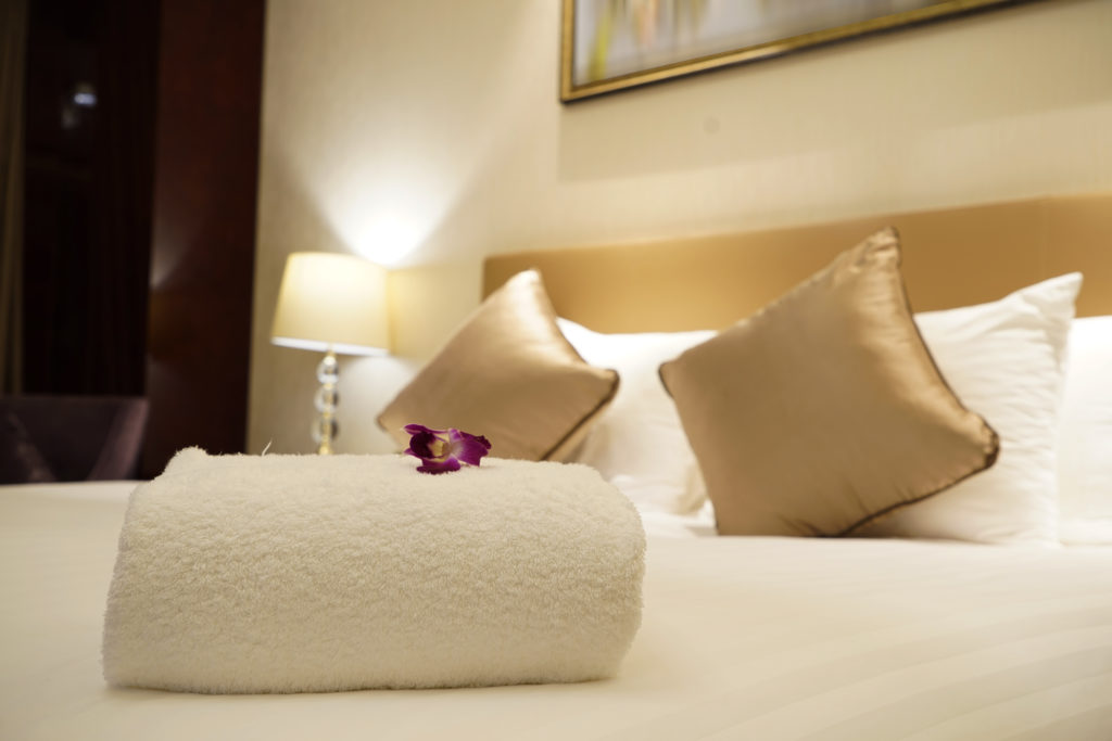 A neatly rolled white towel placed on a hotel bed with an orchid flower on top. - International Hotel School