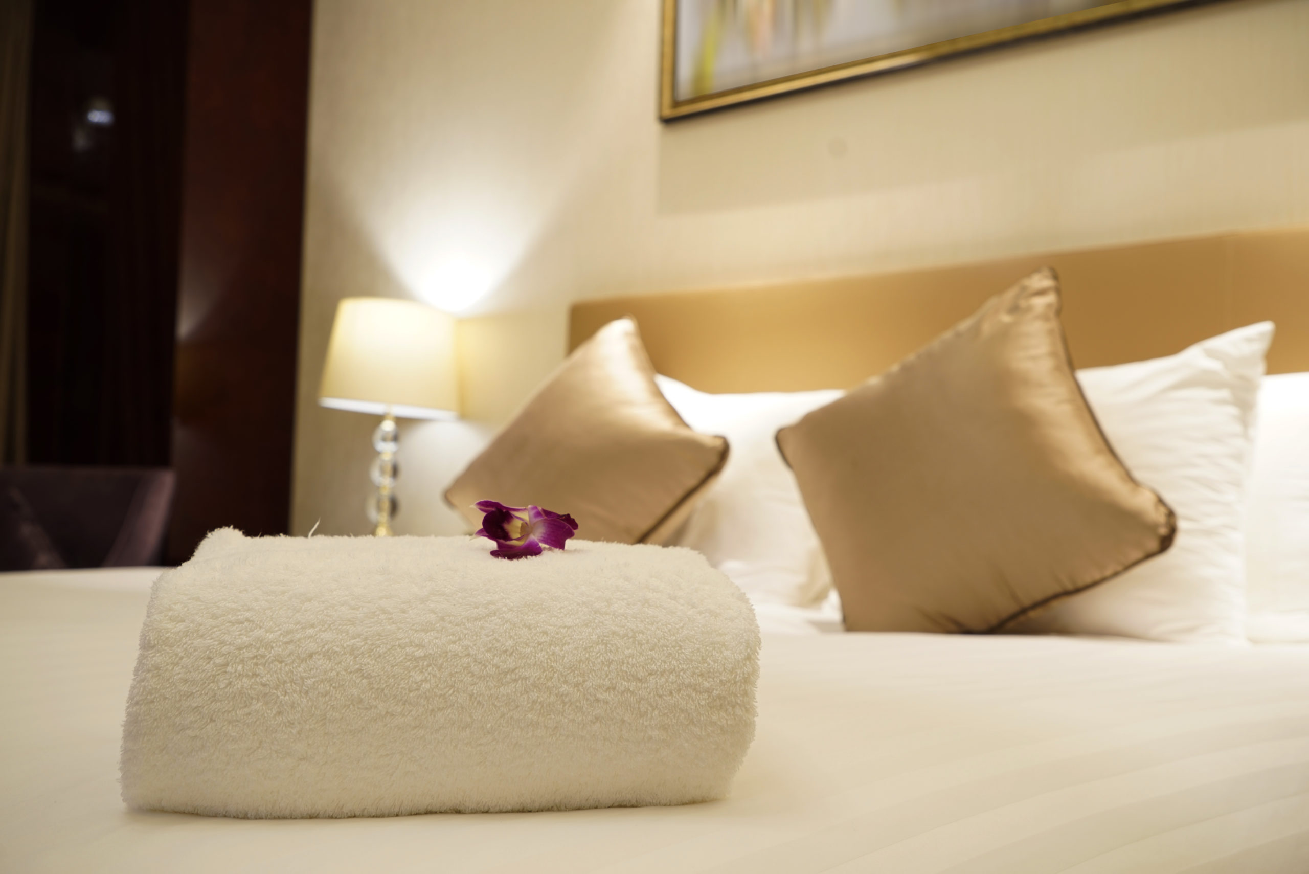 A neatly rolled white towel placed on a hotel bed with an orchid flower on top. - International Hotel School