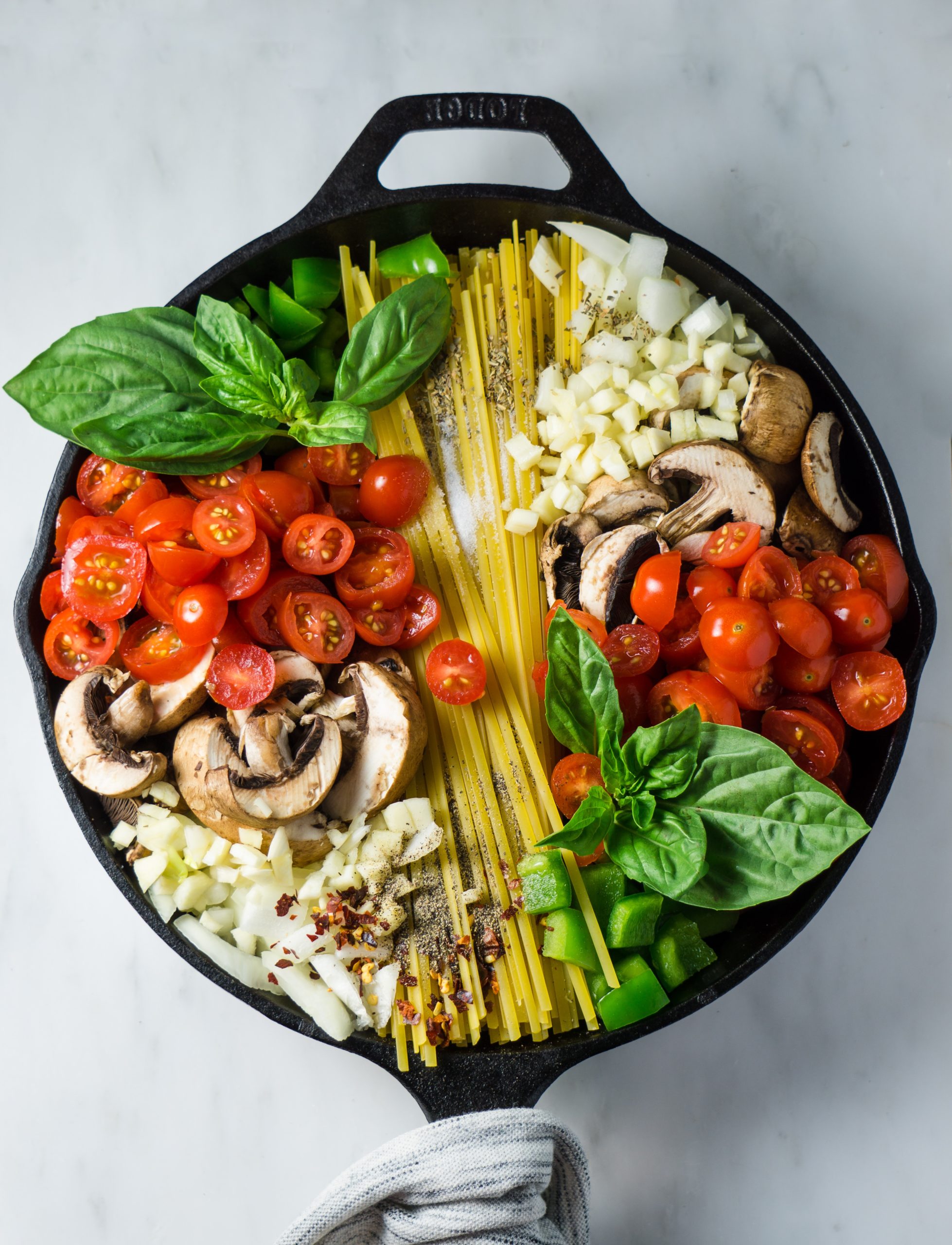 A cast iron skillet filled with pasta, cherry tomatoes, mushrooms, and fresh basil leaves. - International Hotel School