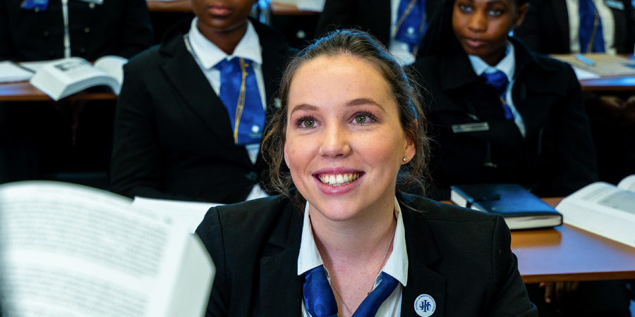 Group of students in a classroom, with one student smiling while engaging with the instructor. - International Hotel School