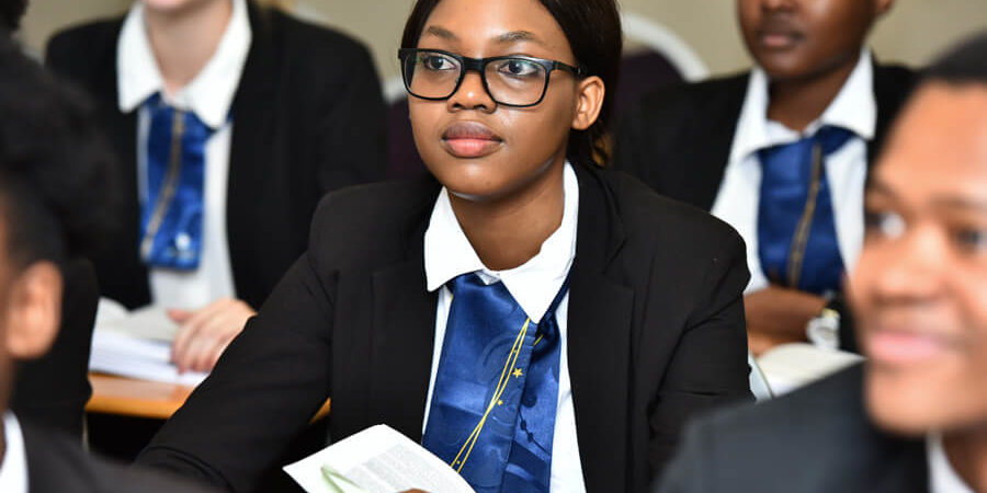 Group of students in a classroom, with one student holding a book and wearing glasses. - International Hotel School