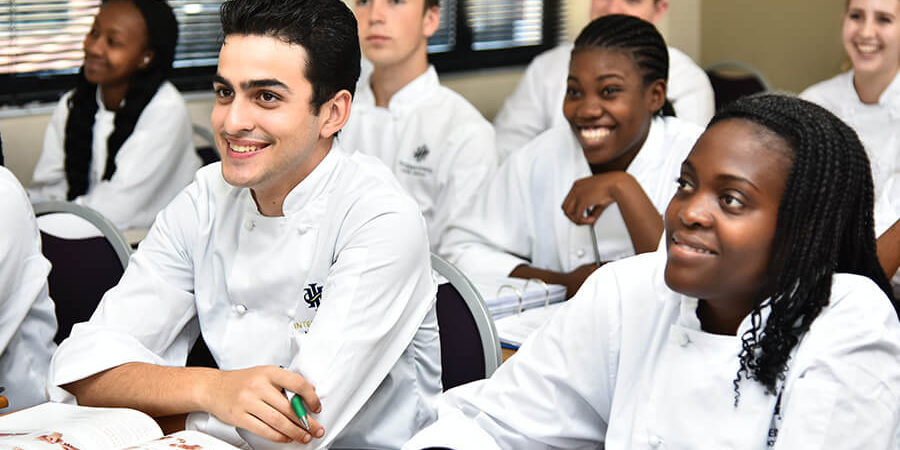 Group of culinary students engaged in a classroom setting, wearing white chef coats. - International Hotel School