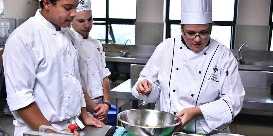 Chef demonstrating cooking techniques to trainees in a culinary training kitchen. - International Hotel School