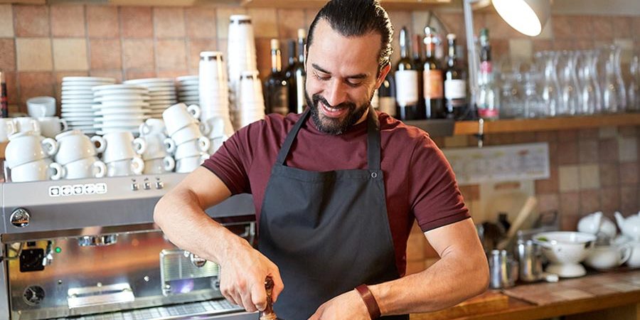 A barista using an espresso machine to prepare coffee in a café setting. - International Hotel School
