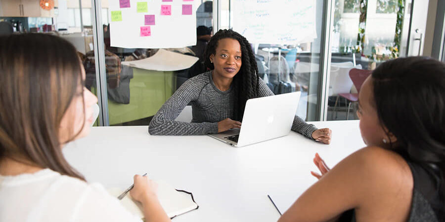 A group of individuals engaged in a business meeting with laptops and notebooks on a table. - International Hotel School