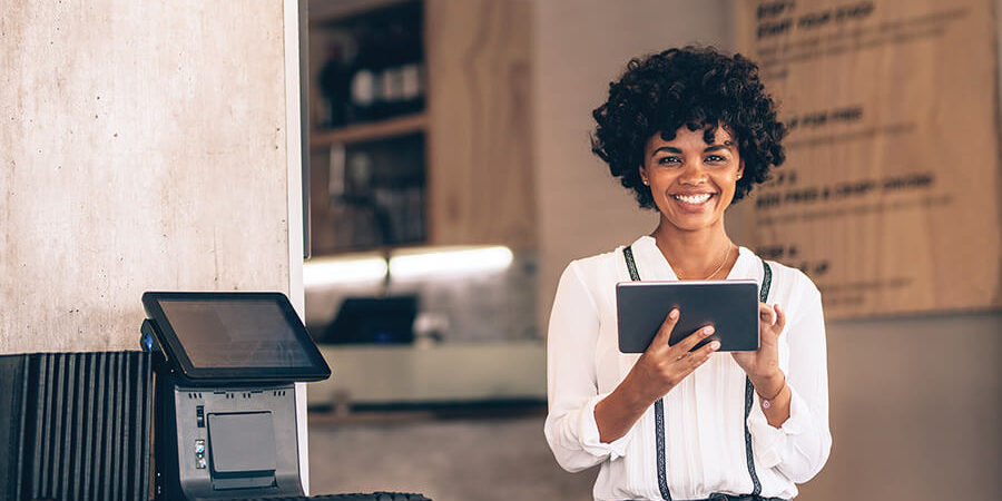 A woman with curly hair holding a tablet and smiling in a hospitality environment. - International Hotel School