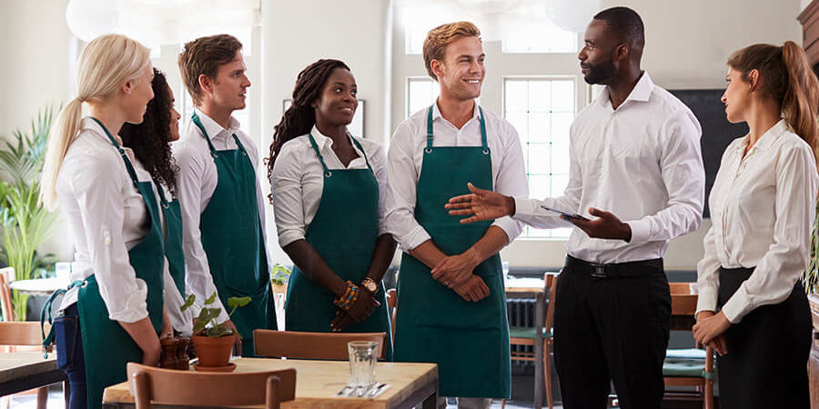 A group of hospitality students wearing aprons engaged in a discussion in a training environment. - International Hotel School