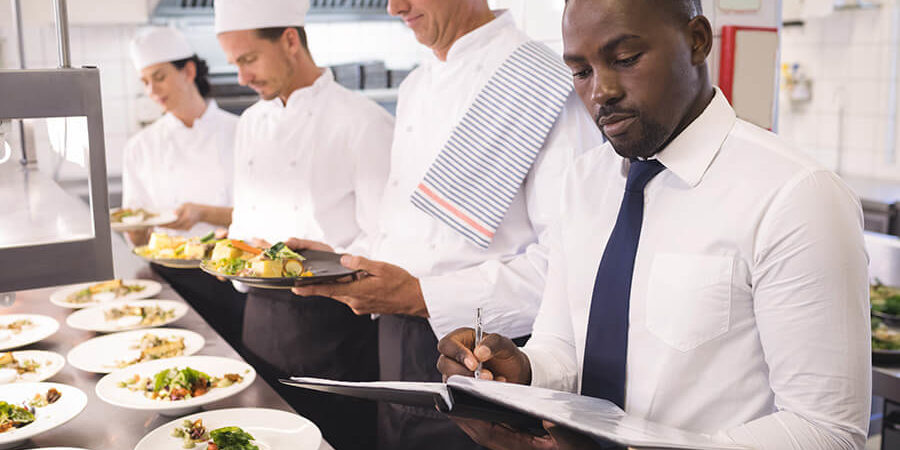A group of culinary professionals in a kitchen preparing and plating dishes. - International Hotel School