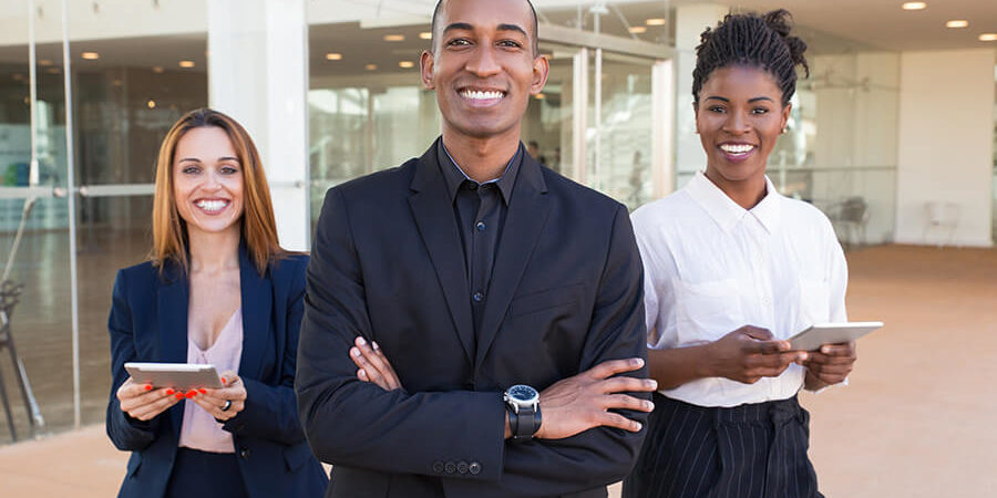Three individuals in business attire standing together, smiling, with one holding a tablet. - International Hotel School