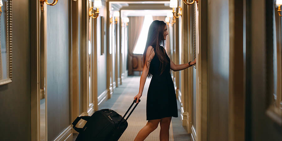 A woman in a black dress pulling a suitcase through a hotel corridor with elegant lighting. - International Hotel School