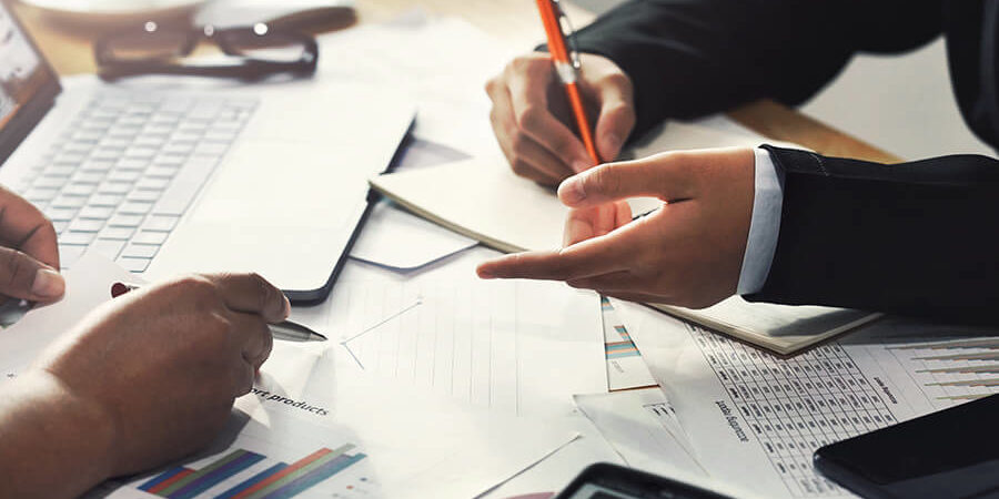 Hands of two individuals discussing financial documents and using a calculator on a table. - International Hotel School