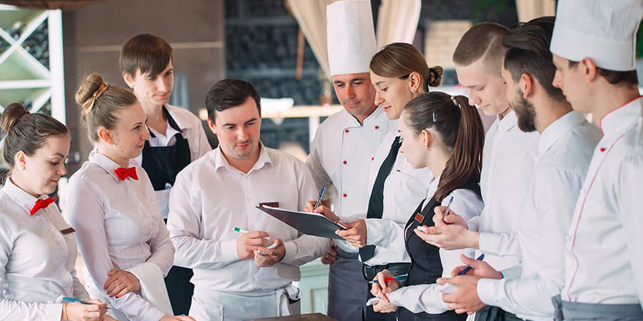 A group of hospitality students in white uniforms discussing in a training environment. - International Hotel School