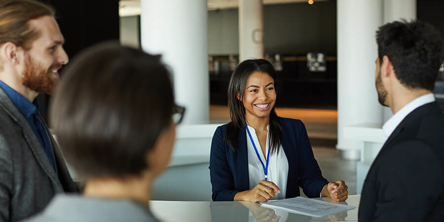 A receptionist smiling and assisting guests at a hospitality front desk in a modern setting. - International Hotel School