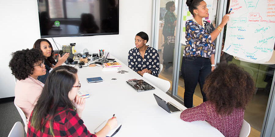 A group of individuals engaged in a meeting with a presentation on a whiteboard in a modern office environment. - International Hotel School