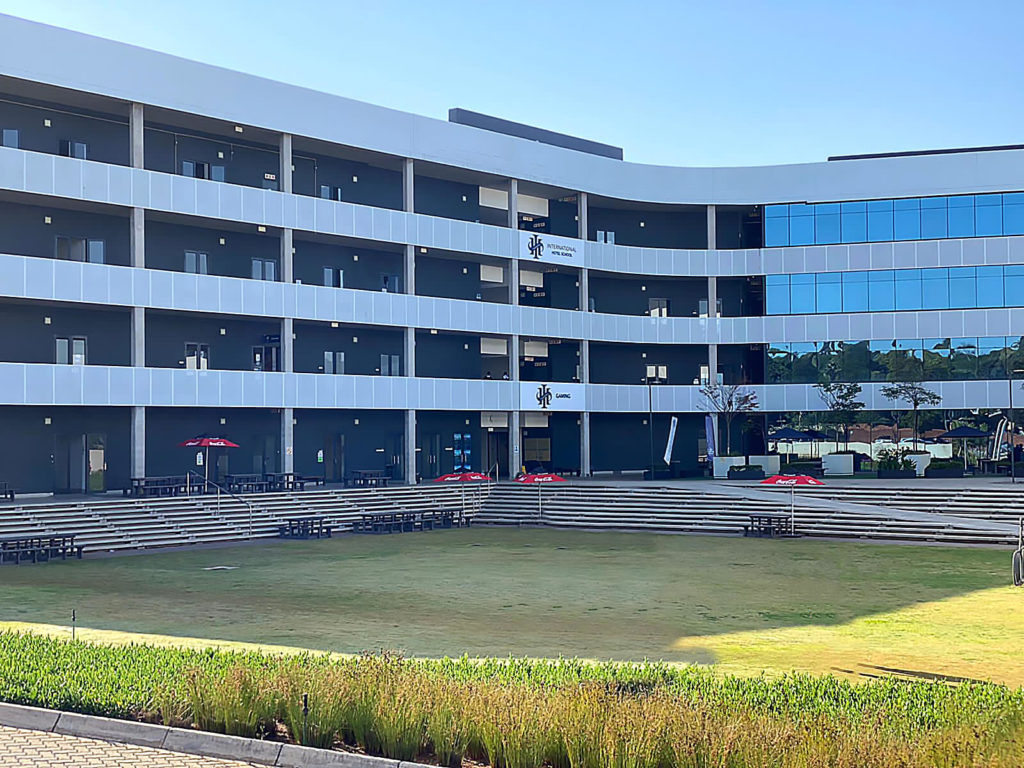 Exterior view of a modern educational building with multiple levels and a central courtyard. - International Hotel School