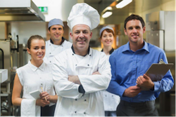 A culinary team posing together in a professional kitchen setting, showcasing chefs and staff. - International Hotel School