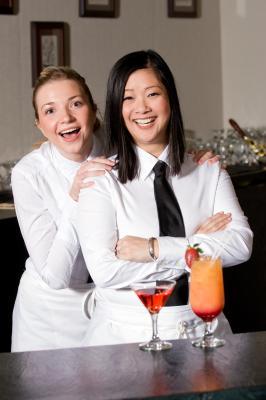 Two waitstaff in formal attire smiling at the camera with cocktails on the bar in front of them. - International Hotel School