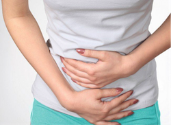 Individual with hands on stomach, indicating discomfort or pain in the abdominal area. - International Hotel School