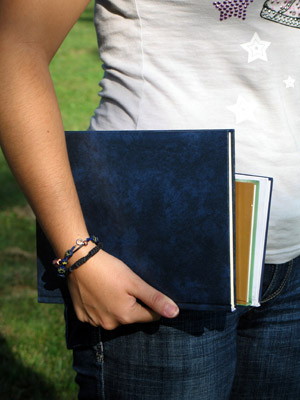 A student holding a stack of notebooks and folders in one hand, wearing a bracelet. - International Hotel School