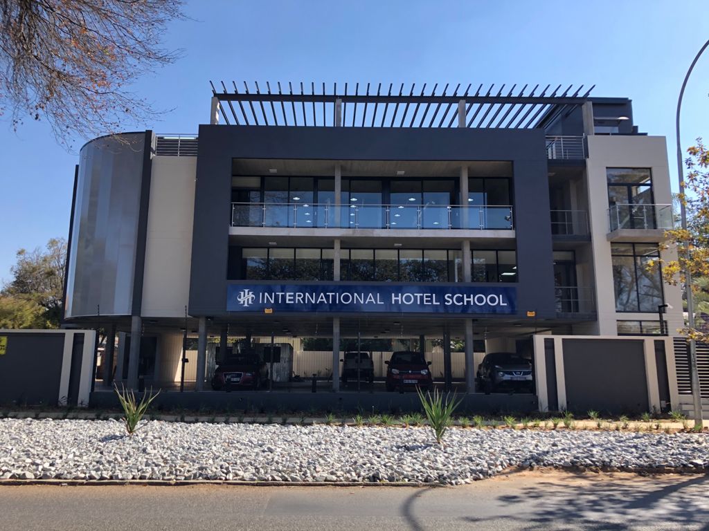 Modern building of the International Hotel School with a prominent sign and glass facade. - International Hotel School