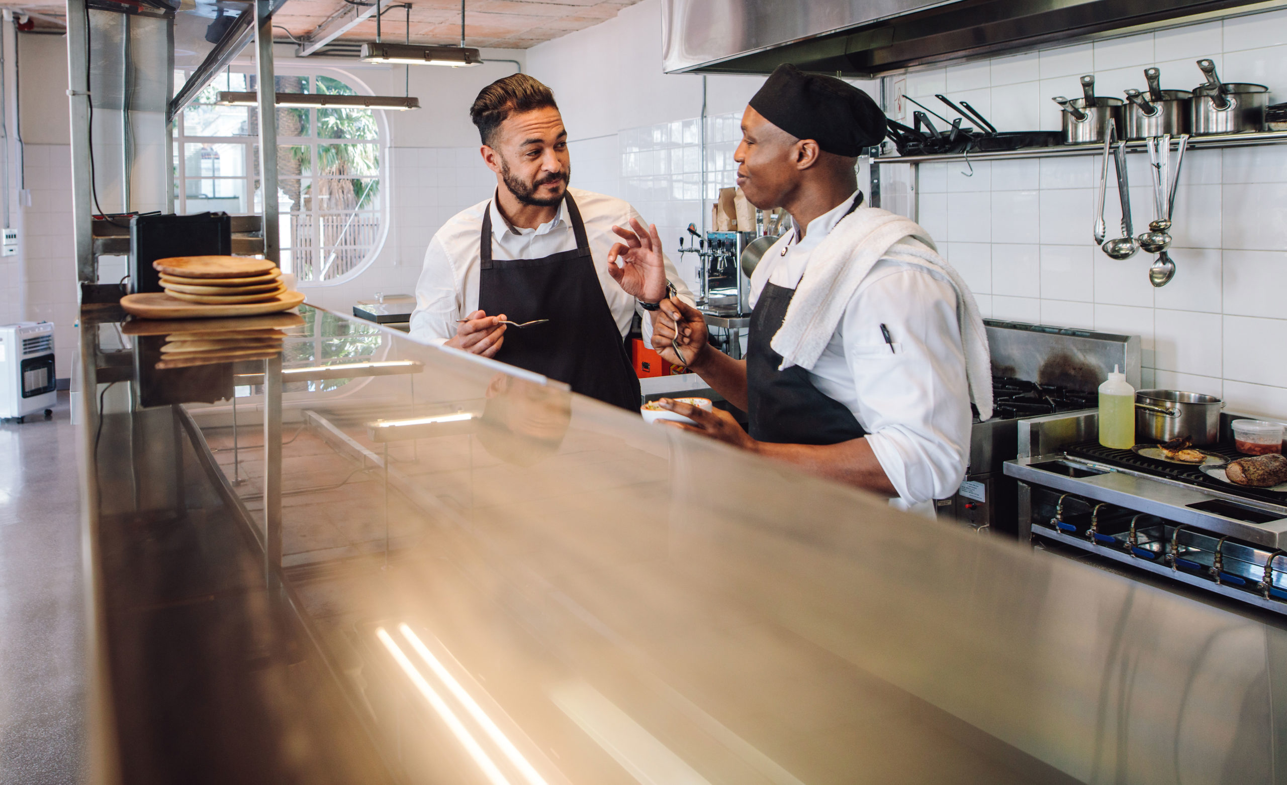 Two chefs discussing in a modern kitchen with cooking equipment and utensils visible. - International Hotel School