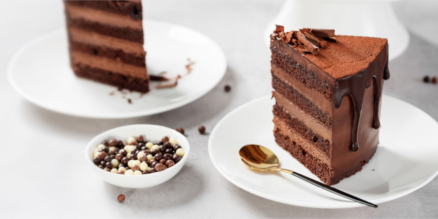 Slice of chocolate layer cake with chocolate ganache and decorative chocolate shavings on a plate. - International Hotel School