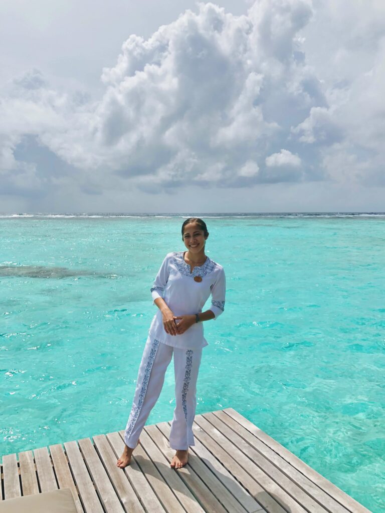 Woman wearing a white outfit standing on a wooden deck over turquoise water. - International Hotel School