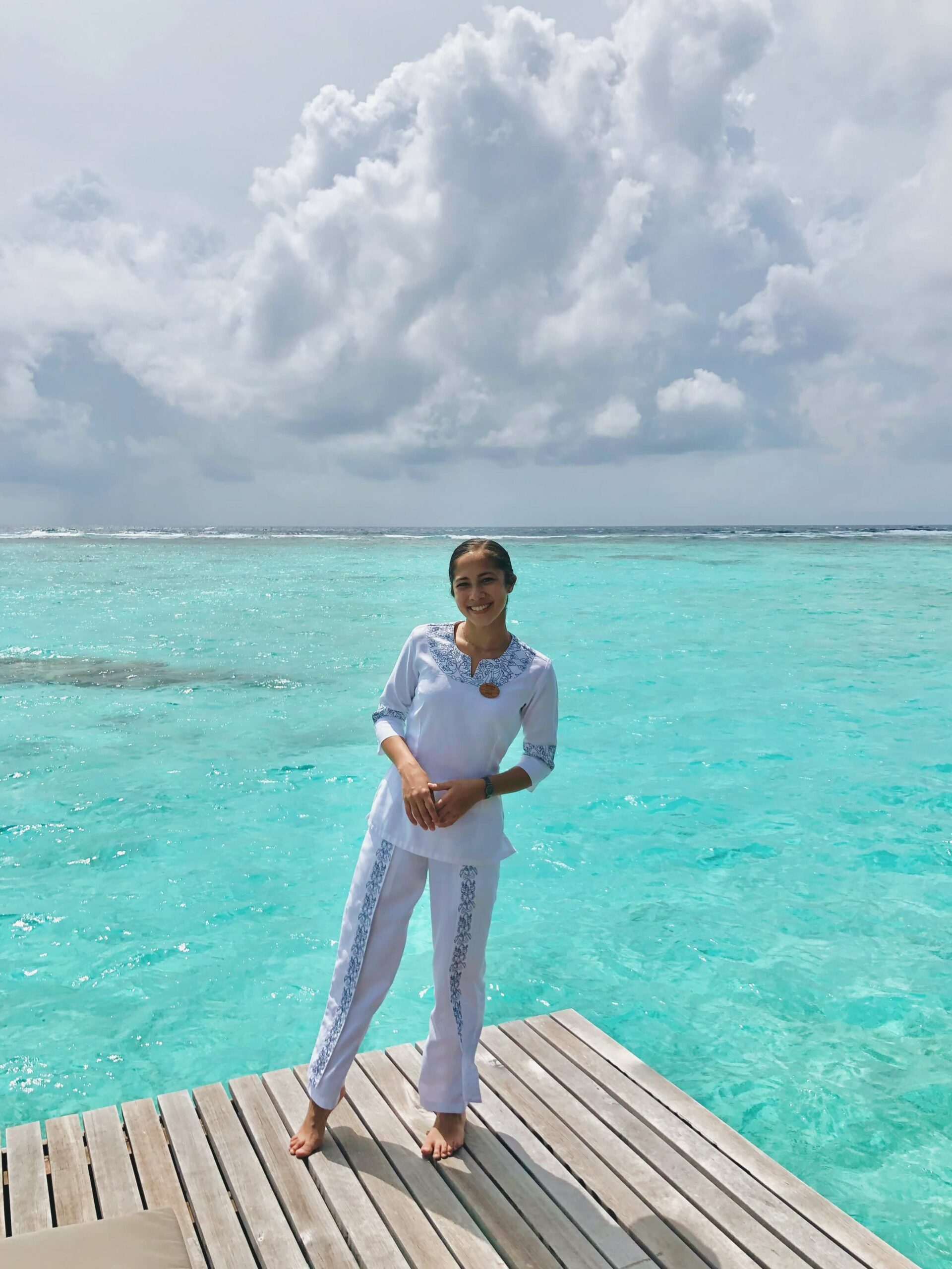 Woman wearing a white outfit standing on a wooden deck over turquoise water. - International Hotel School