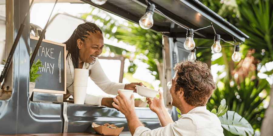 Customer receiving food from a vendor at a food truck with a takeaway sign. - International Hotel School