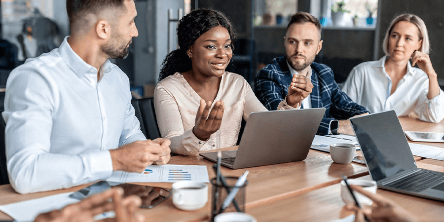 A diverse group of professionals engaged in a discussion around a table with laptops and documents. - International Hotel School