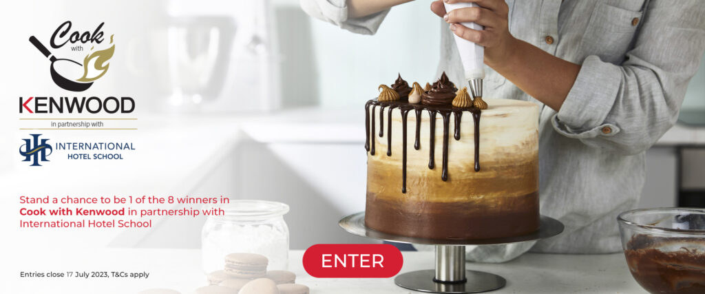 A person decorating a multi-layered cake with chocolate icing and pastry cream in a kitchen setting. - International Hotel School
