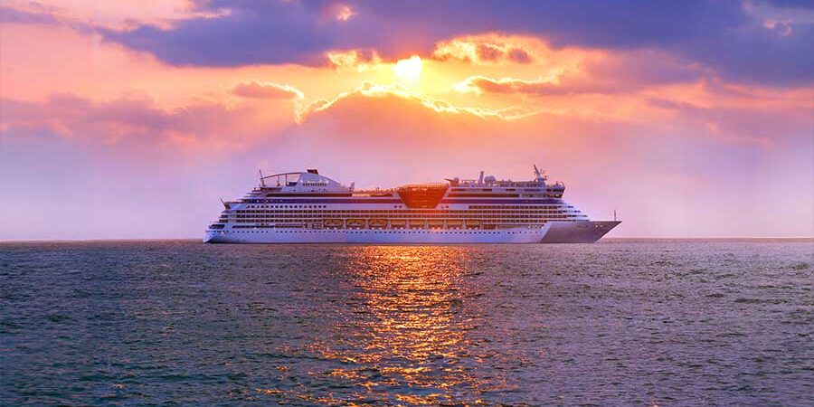 A cruise ship sailing on calm waters during a vibrant sunset with clouds and reflections. - International Hotel School